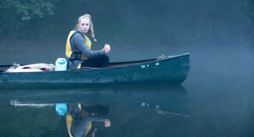 A person wearing a life jacket sits in a canoe in fog. 